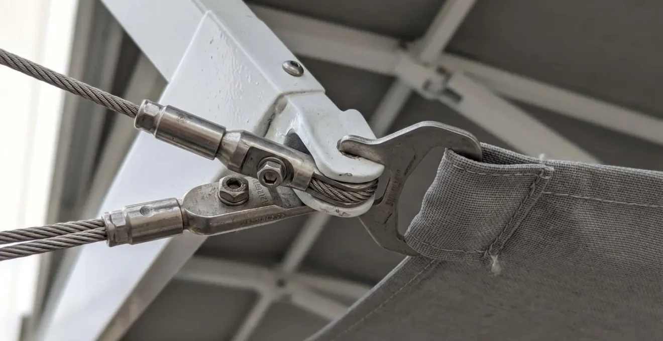 Gros plan sur la jonction entre l'armature aluminium thermolaqué blanc et les bras à câbles doubles d'un store double pente