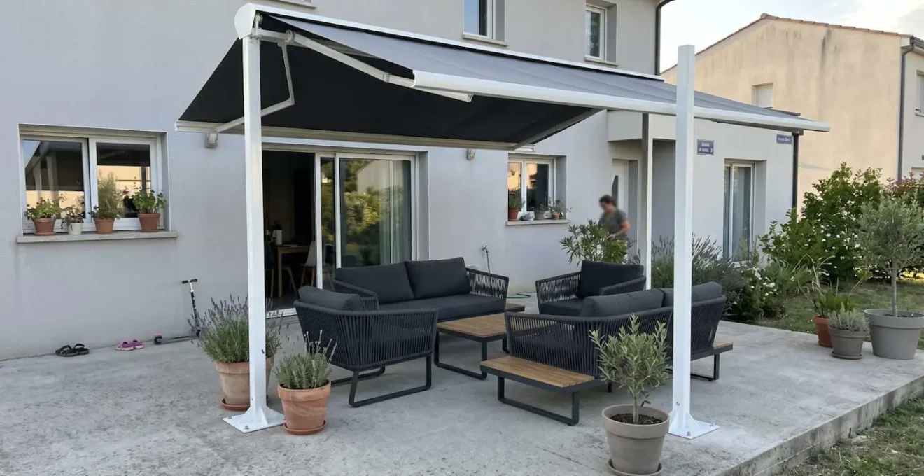 Store double pente en configuration îlot sur quatre poteaux aluminium blancs avec platines de fixation visibles sur terrasse privée en béton
