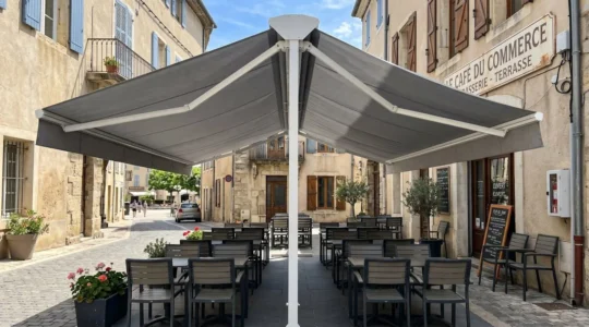 Terrasse de café contemporain avec store double pente déployé créant deux zones d'ombre symétriques sous armature aluminium blanche