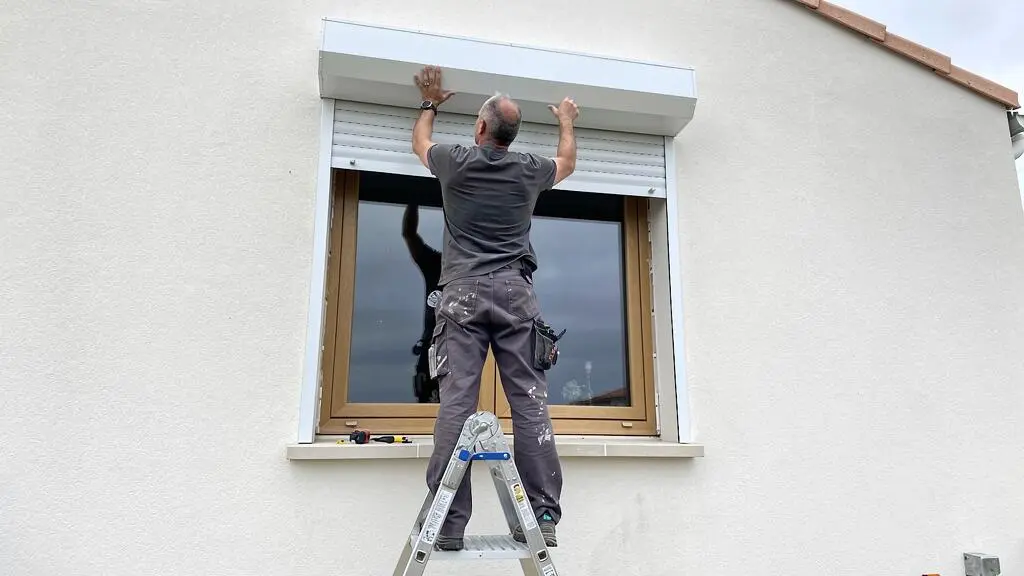Menuisier installant un coffre de volet roulant au-dessus d'une fenêtre sur une façade vendéenne